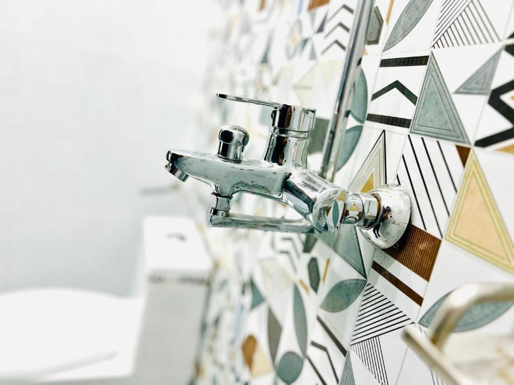 a bathroom sink with a tap on a mosaic wall at Sj Luxury Suits in Lahore