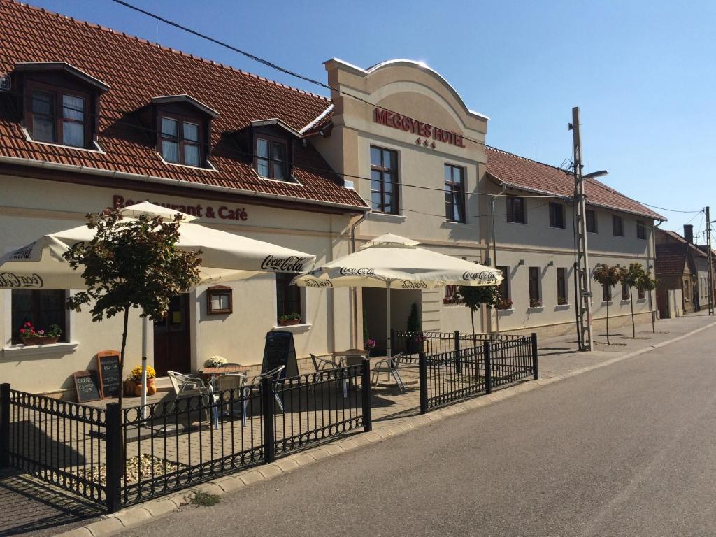 un edificio con mesas y sombrillas en una calle en Meggyes Hotel en Szerencs