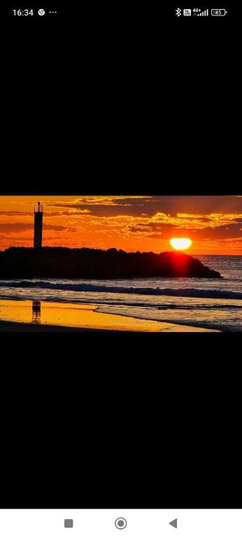 un coucher de soleil sur une plage avec un phare dans l'océan dans l'établissement studio au cap d'agde dans les pinèdes, au Cap d'Agde