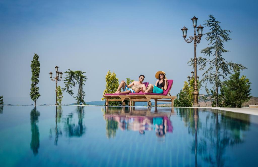 Dos personas sentadas en sillas junto a una piscina en Shamakhi Palace Sharadil, en Şǝrǝdil