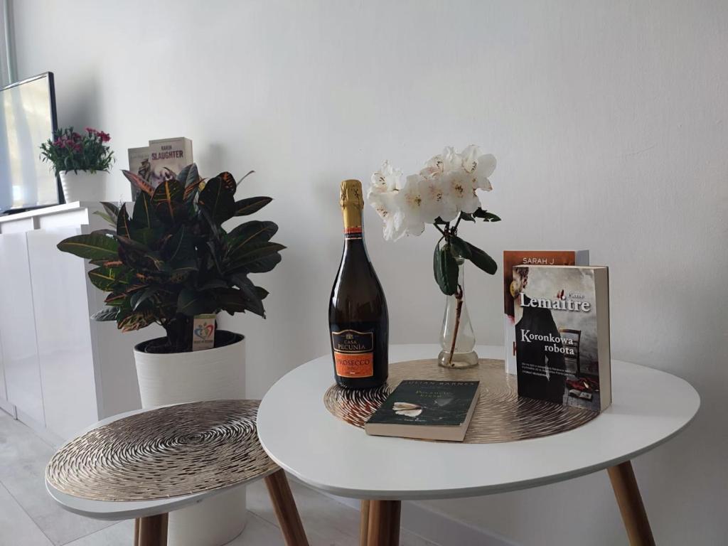 a bottle of wine on a table with a book and flowers at Kawalerka apartament ul gieldowa in Kołobrzeg