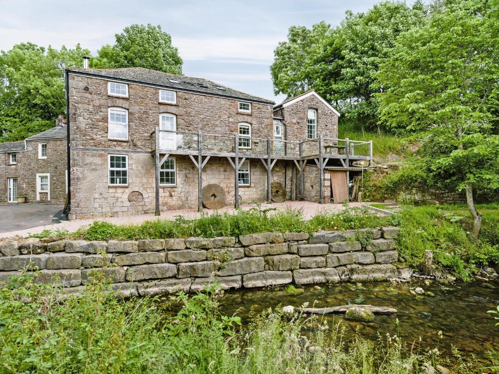 an old brick house with a stone wall next to a pond at The Old Mill in Hackthorpe