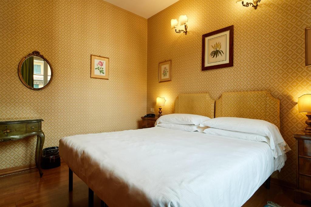 a bedroom with a bed with white sheets and a mirror at Hotel Hermitage in Florence