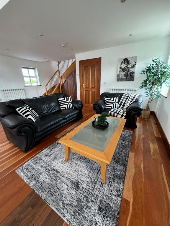 a living room with black leather couches and a coffee table at De Búrca Cottage KERRY in Brackhill