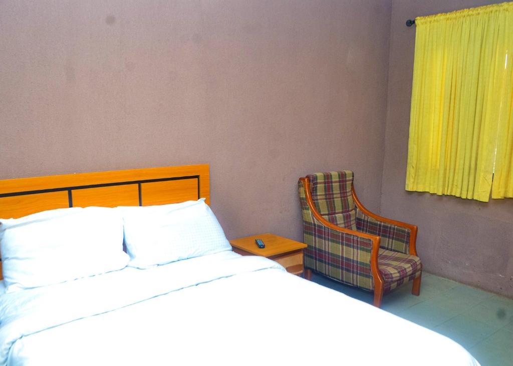 a bedroom with a bed and a chair and a window at Miccom Golf Hotel and Resort in Ikirun