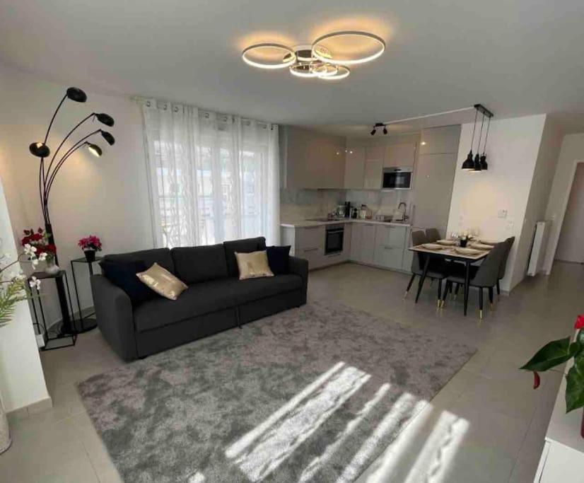 un salon avec un canapé noir et une cuisine dans l'établissement Appartement chaleureux à côté de Disneyland-Paris et Val d Europe, à Chessy
