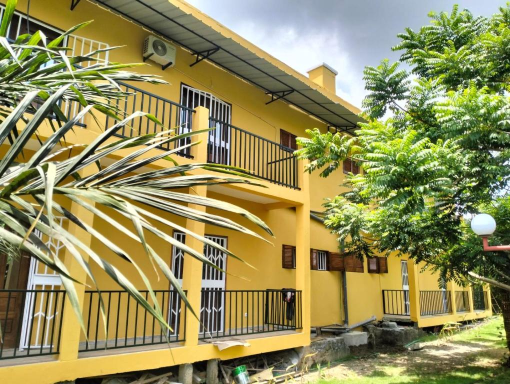 un bâtiment jaune avec des balcons noirs et des arbres dans l'établissement Moradia Turistica MJ ROOMS CITY, à São Tomé