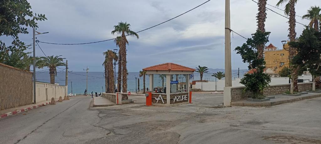 a bus stop on a street with palm trees and the ocean at Perle in Aïn El Turk