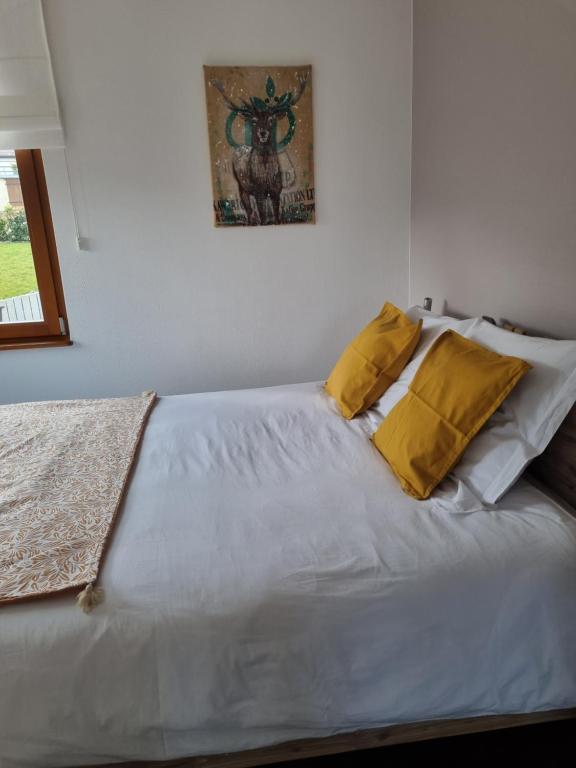 ein weißes Bett mit gelben Kissen darüber in der Unterkunft Gîte chez Alice in Mollkirch