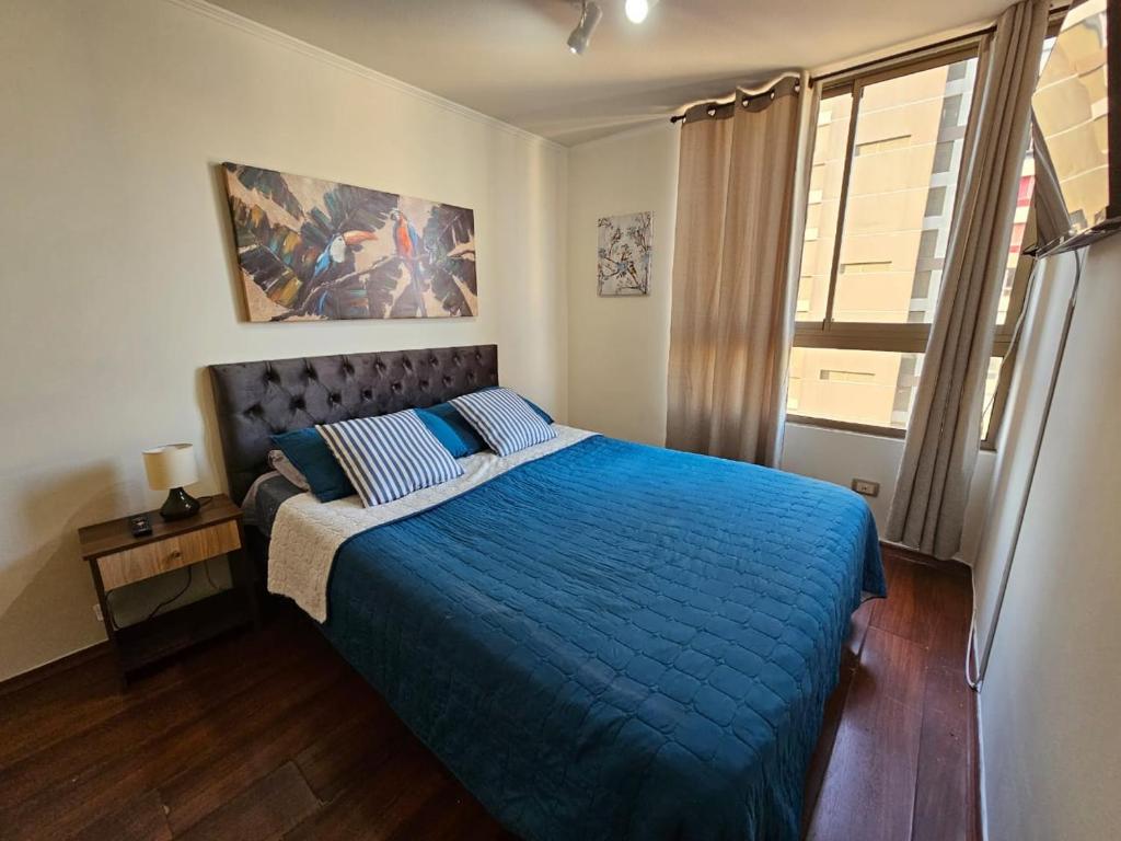 a bedroom with a bed with a blue comforter and a window at departamentos santiago centro moneda SUAGON APART HOTEL in Santiago