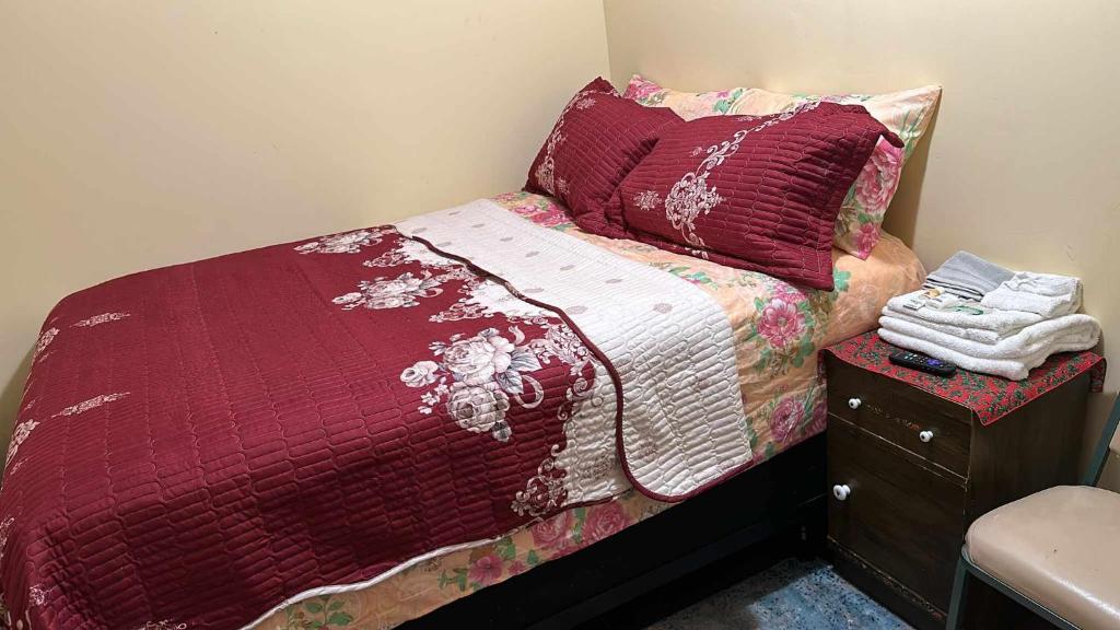 uma pequena cama com um edredão vermelho e uma mesa de cabeceira em Room J Divine Villa and Resorts 5mins to EWR Airport and 4mins to Penn Station Newark, New York em Newark