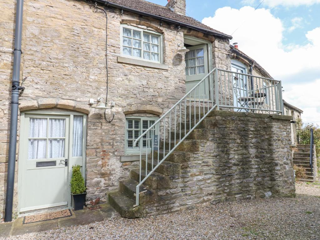 een oud stenen huis met een witte deur en een trap bij In & Out Cottage in Middleham