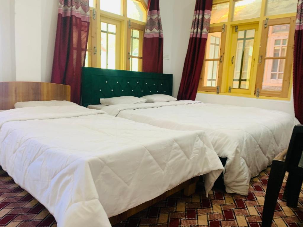 two beds with white sheets in a room with windows at The Gurez inn hotel and restaurant in Kanzalwan