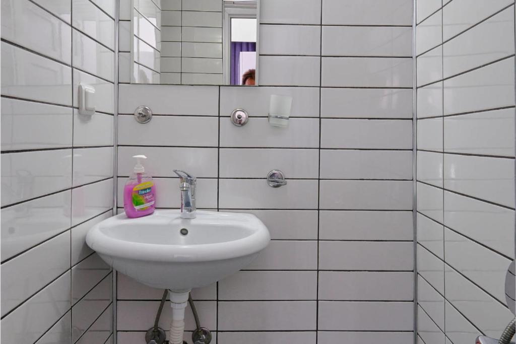 La salle de bains est pourvue de carrelage blanc, d'un lavabo et d'un miroir. dans l'établissement CARETTA PANSİYOn, à Kaş