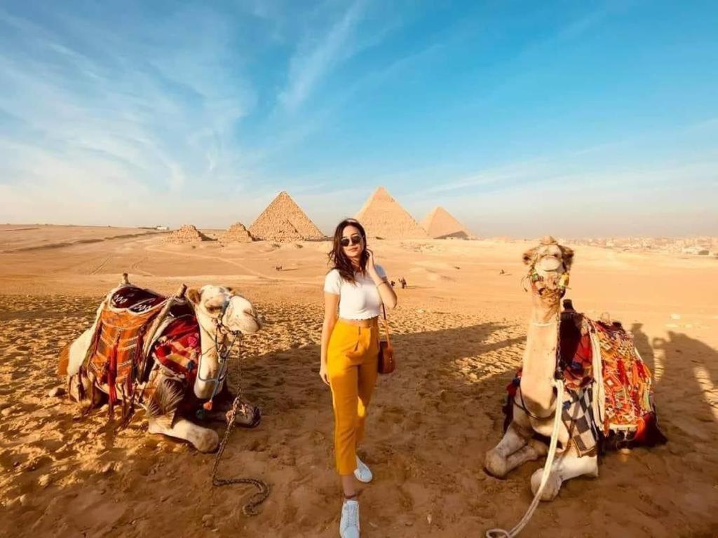 een vrouw die naast twee kamelen in de piramiden staat bij Pyramids Express View Hotel in Caïro
