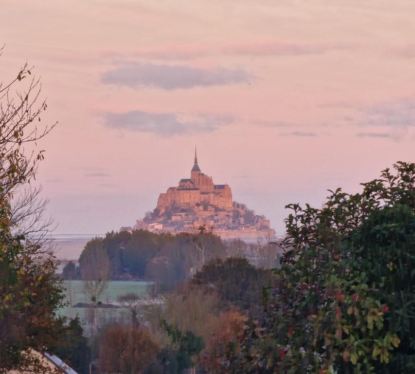 een gebouw bovenop een heuvel met bomen bij L'Aurore de la Baie, vue sur le Mont-Saint-Michel in Huisnes-sur-Mer