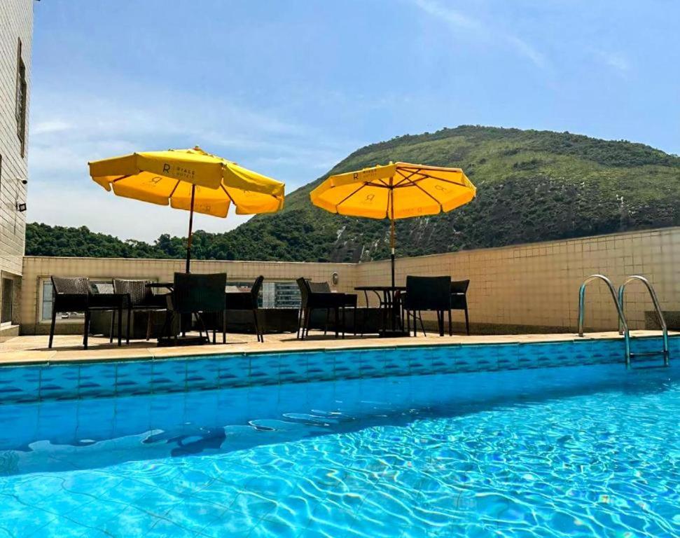 a swimming pool with two umbrellas and tables and chairs at Riale Vilamar Copacabana in Rio de Janeiro