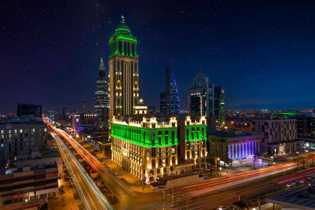 Narcissus Riyadh Hotel & Spa في الرياض: مبنى مضاء مع أضواء خضراء على مدينة في الليل