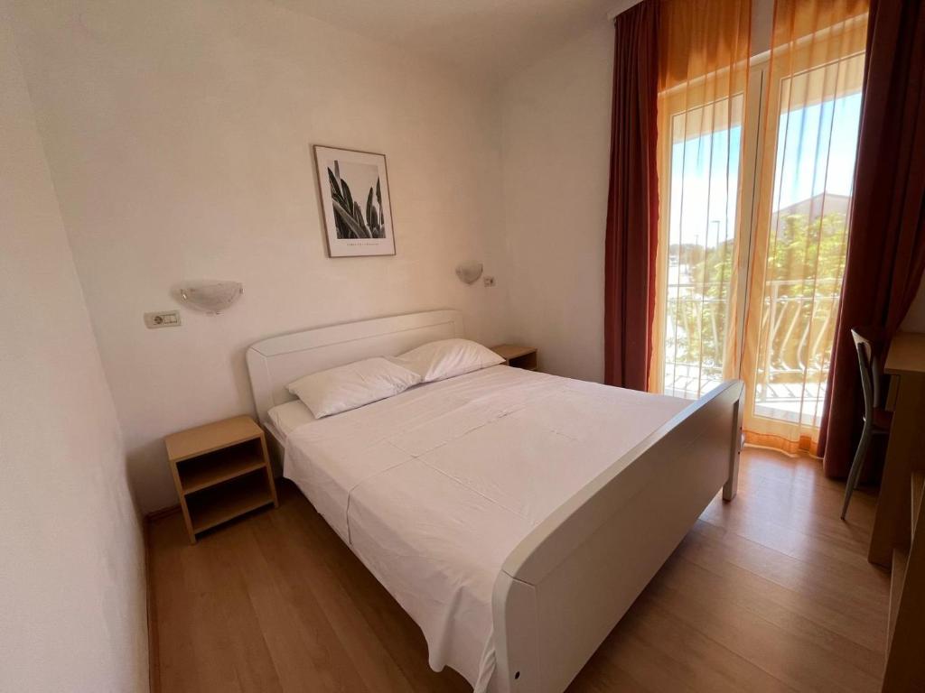 a bedroom with a white bed and a large window at Apartmani Šaldi in Pakoštane