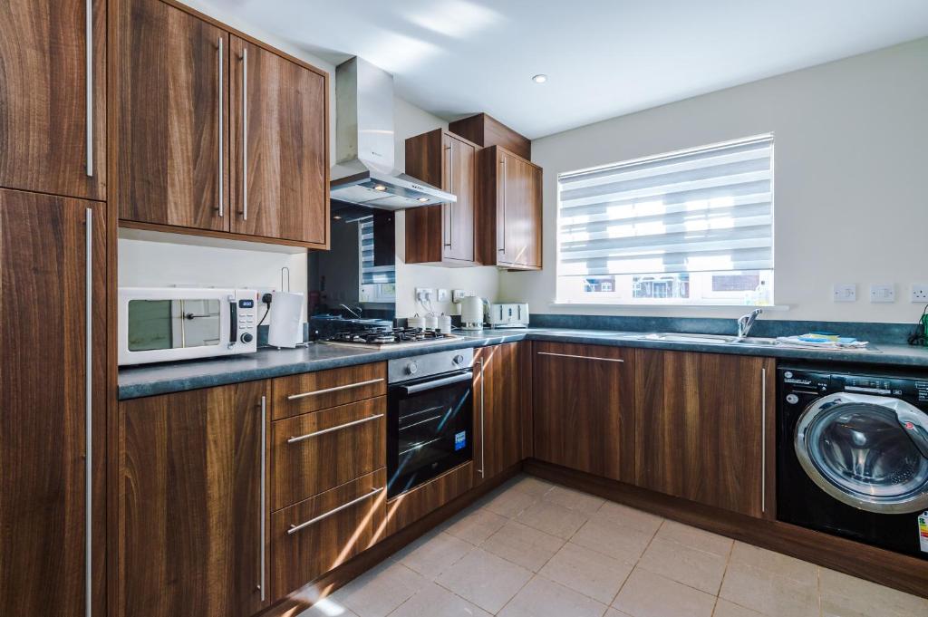 a kitchen with wooden cabinets and a washer and dryer at Modern Semi detached in a quiet location, Driveway parking in Ewloe