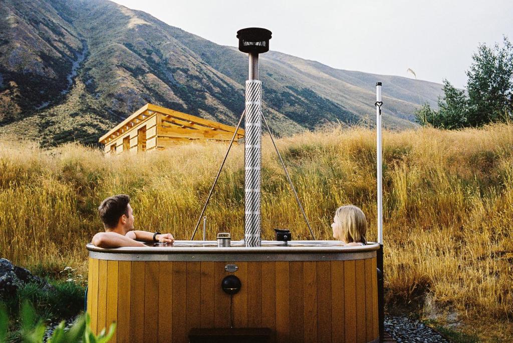 Te Manahuna Retreat في تويزل: شخصان في حوض استحمام خشبي في حقل