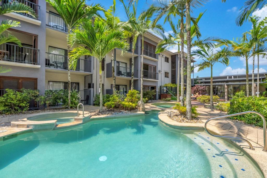 a swimming pool with palm trees in front of a building at Southern Cross Escape in Cairns