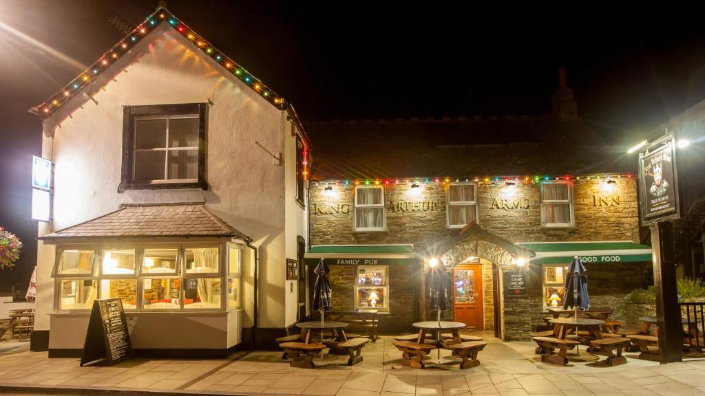 un edificio con mesas de picnic delante de él por la noche en King Arthurs Arms en Tintagel