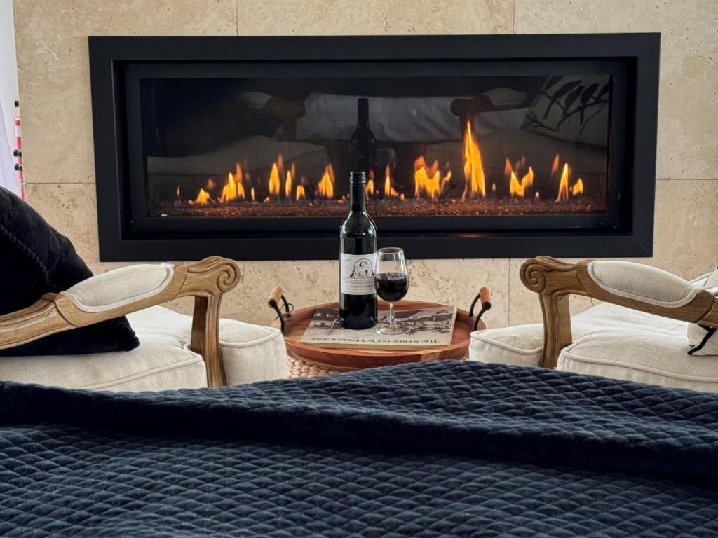 a fireplace with a bottle of wine and two chairs at Luxury winter escape with Mountain Views by Scotch Hill Truffle Farm in Neerim South