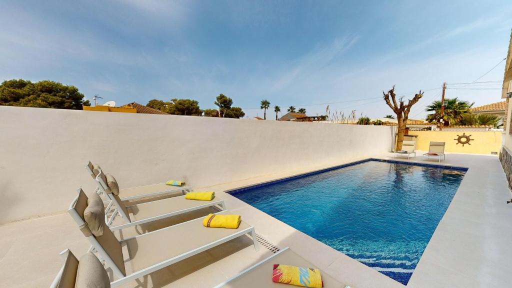 einen Pool mit zwei Stühlen neben einer weißen Wand in der Unterkunft Villa Greenland-A Murcia Holiday Rentals Property in Los Alcázares