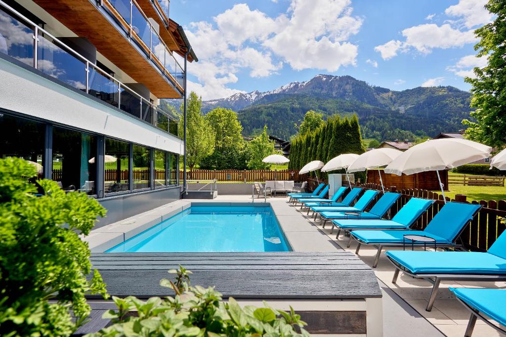 einen Pool in einem Hotel mit Liegestühlen und Sonnenschirmen in der Unterkunft HOTEL SONNBLICK Kaprun Salzburg - incl Zell am See-Kaprun Summercard in Kaprun