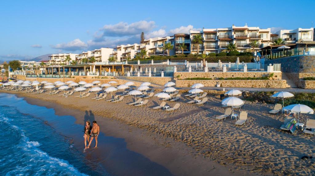 uma praia com um monte de guarda-sóis e pessoas na praia em Alexander Beach Hotel & Village Resort em Mália
