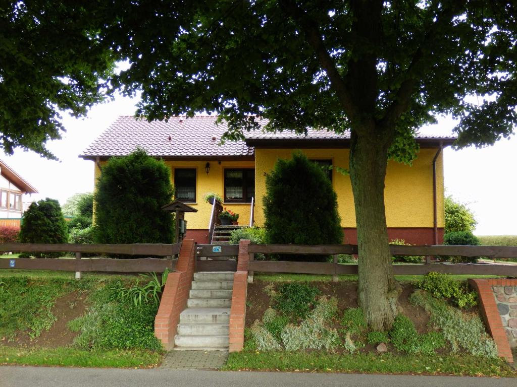 Una casa amarilla con un árbol delante. en Ferienwohnung unweit der Müritz en Gotthun