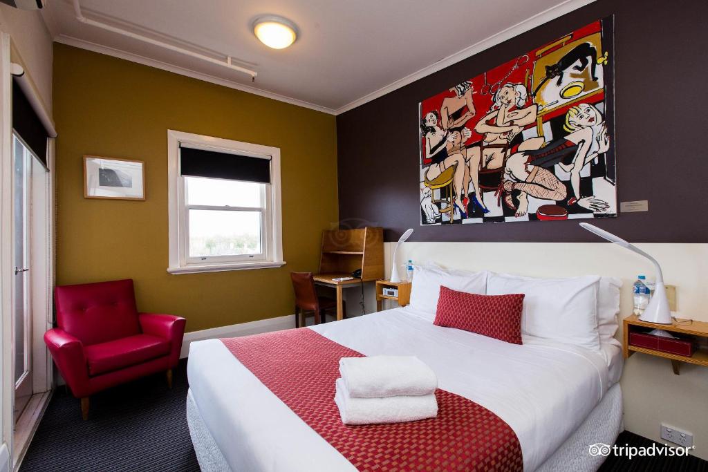 Tolarno Hotel - Chambre Boheme - Australia في ملبورن: غرفة نوم بسرير كبير وكرسي احمر