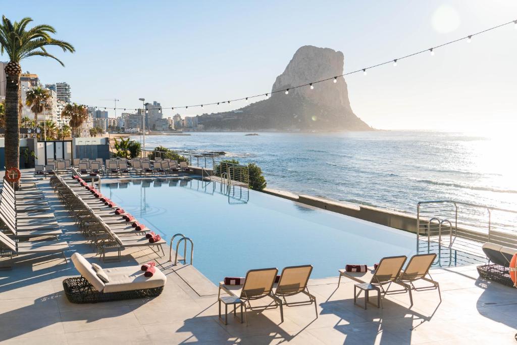 a swimming pool with chairs and a view of the ocean at ESTIMAR Calpe Apartments in Calpe