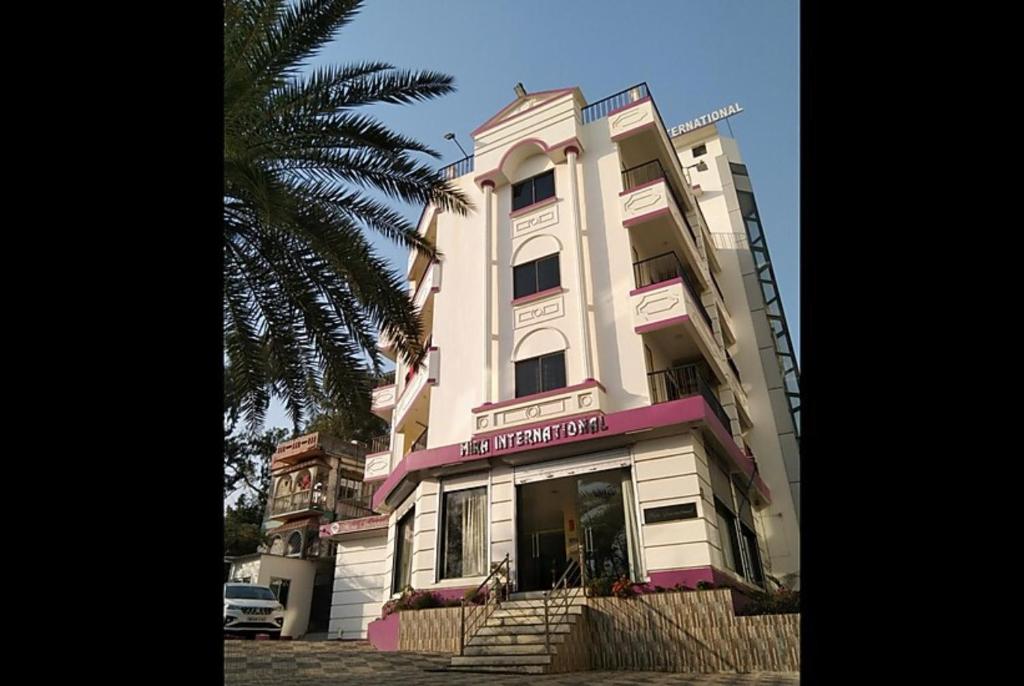 Hotel Mira international - Luxury Stay - Best Hotel in digha في ديغا: مبنى أبيض طويل مع تقليم وردي