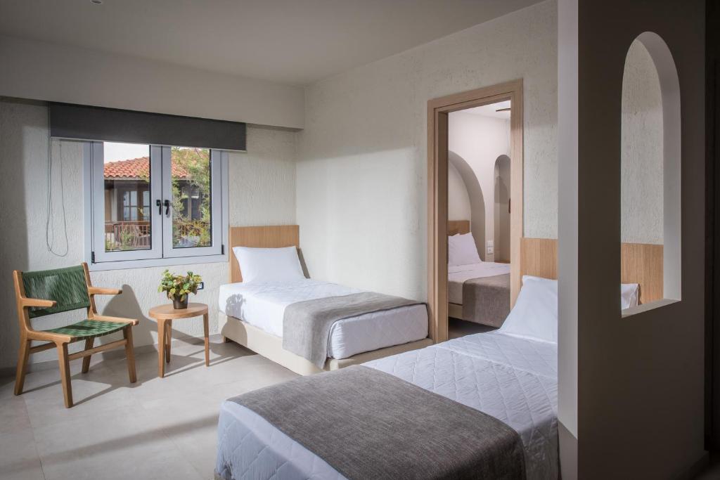 a bedroom with two beds and a chair and a mirror at South Coast Hotel in Makry Gialos