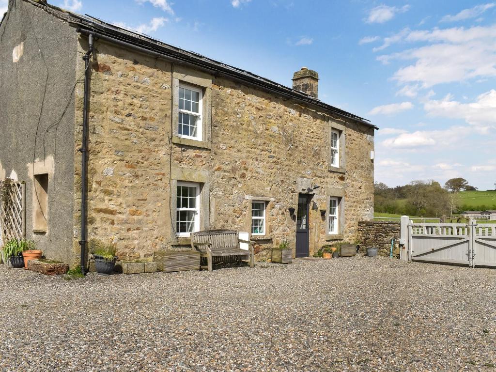 una vieja casa de piedra con un banco delante de ella en Box Tree Farmhouse - Uk47034 en Kirkby Lonsdale