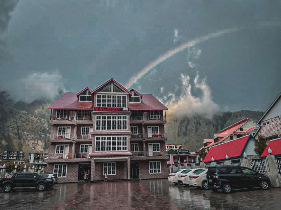 um arco-íris sobre um edifício com carros estacionados na chuva em Magnum Hotel em Battakundi
