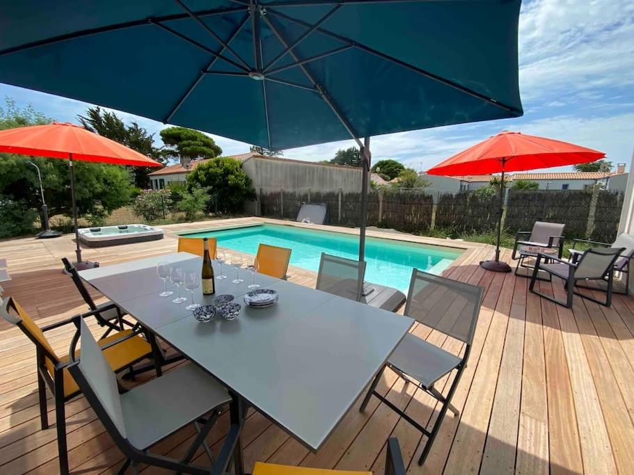 een patio met een tafel, parasols en een zwembad bij Villa Les Sables Vigniers, Piscine et Jacuzzi prives, plage à 800m in Les Sables Vignier