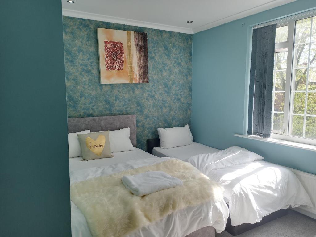 1 dormitorio azul con 2 camas y ventana en An Exquisite Deluxe Room in a Hotel - Free Parking - with access to Resturant - Shisha Bar- Wine Bar, en Roundhay