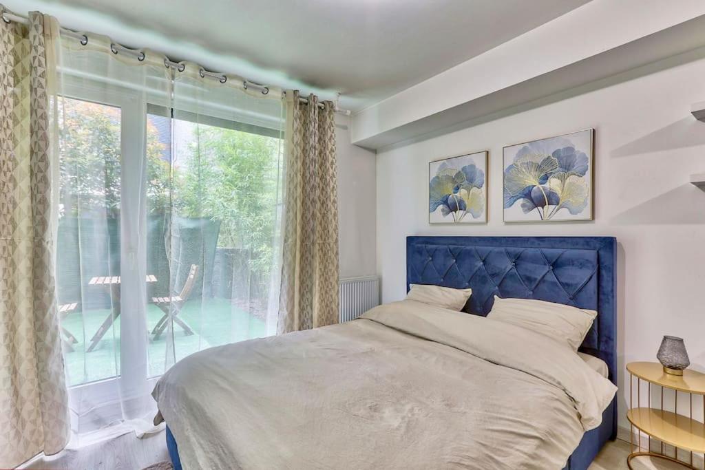une chambre avec un lit bleu et une grande fenêtre dans l'établissement Joli studio avec jardin près de Paris, à Romainville