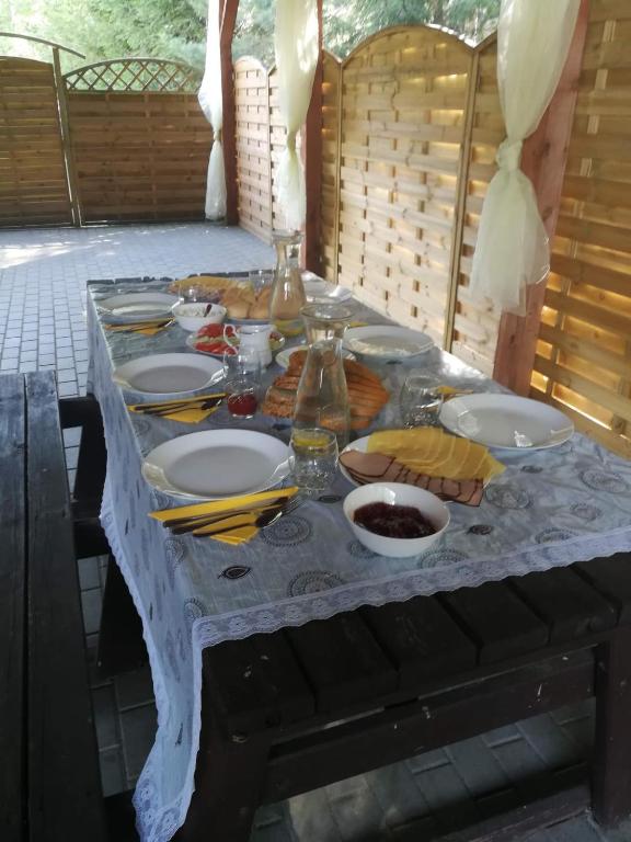 Outdoor table set with plates, cutlery, and food under a wooden canopy.