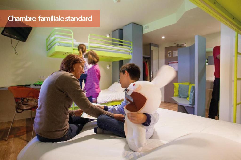 a man and woman sitting on a bed with a stuffed animal at Hôtel du Futuroscope in Jaunay-Marigny