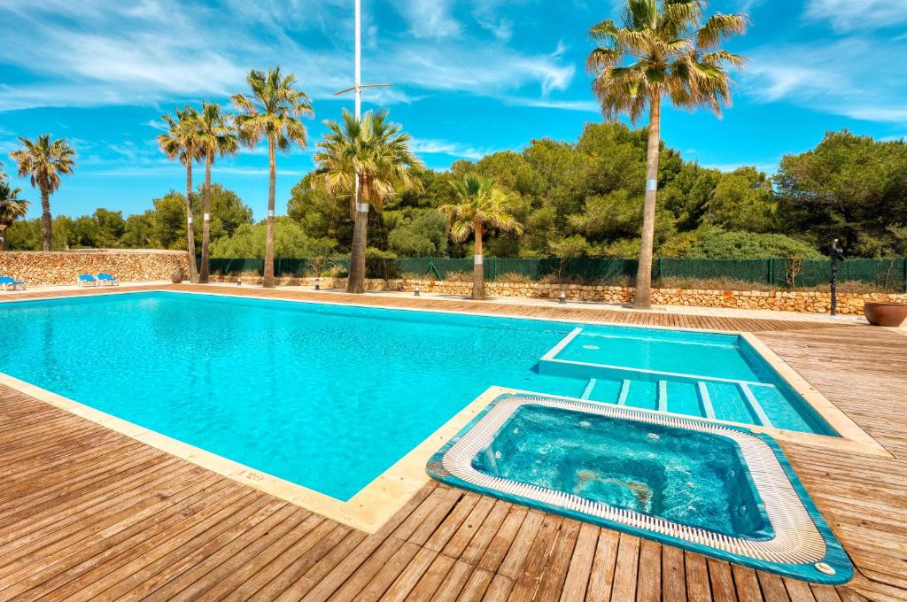a swimming pool with a wooden deck and palm trees at Acogedor Duplex en Ciutadella-Playa Santandria in Cala Santandria