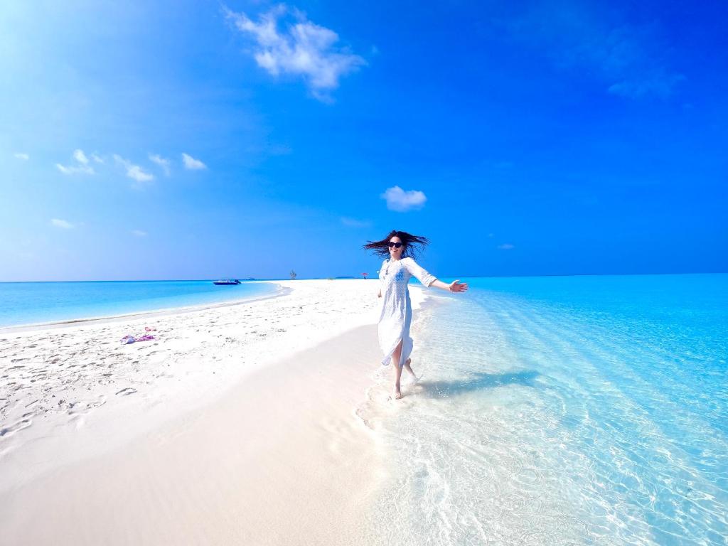 Una donna in abito bianco che cammina su una spiaggia di Wind Breeze Sunset View Inn a Guraidhoo