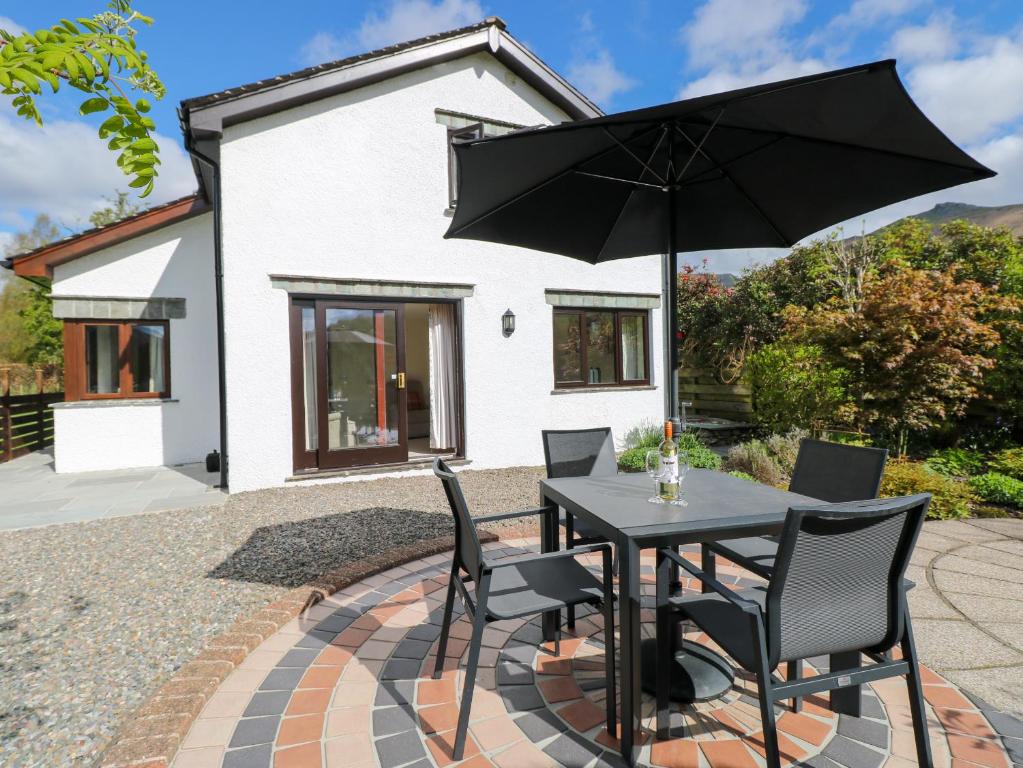 einem schwarzen Tisch mit Stühlen und einem Sonnenschirm auf einer Terrasse in der Unterkunft Rowanberry Cottage in Grasmere