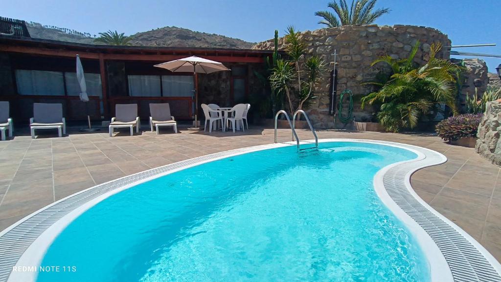 einen Pool in einem Garten mit Stühlen und einem Sonnenschirm in der Unterkunft ANFI TOPAZ VILLA TAURO GOLF & BEACH 3 bedrooms 4 bathrooms private pool in Mogán