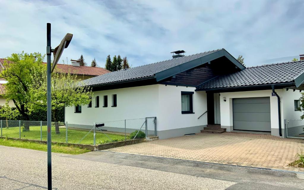 una casa bianca con garage e recinzione di GARDEN PARADISE - Ferienhaus mit 400m2 Garten - Nähe Ossiacher See a Villach