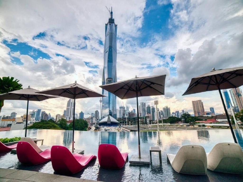 a pool with chairs and umbrellas in front of a city at Opus Residence Kuala Lumpur by KL Suite in Kuala Lumpur