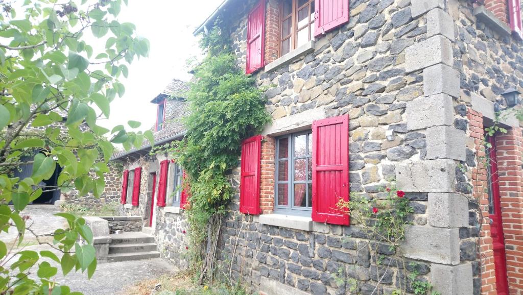 an old stone building with red windows and ivy at En pleine nature cantalienne et au calme village , Maison confortable et spacieuse pour 9 pers in Vezels-Roussy